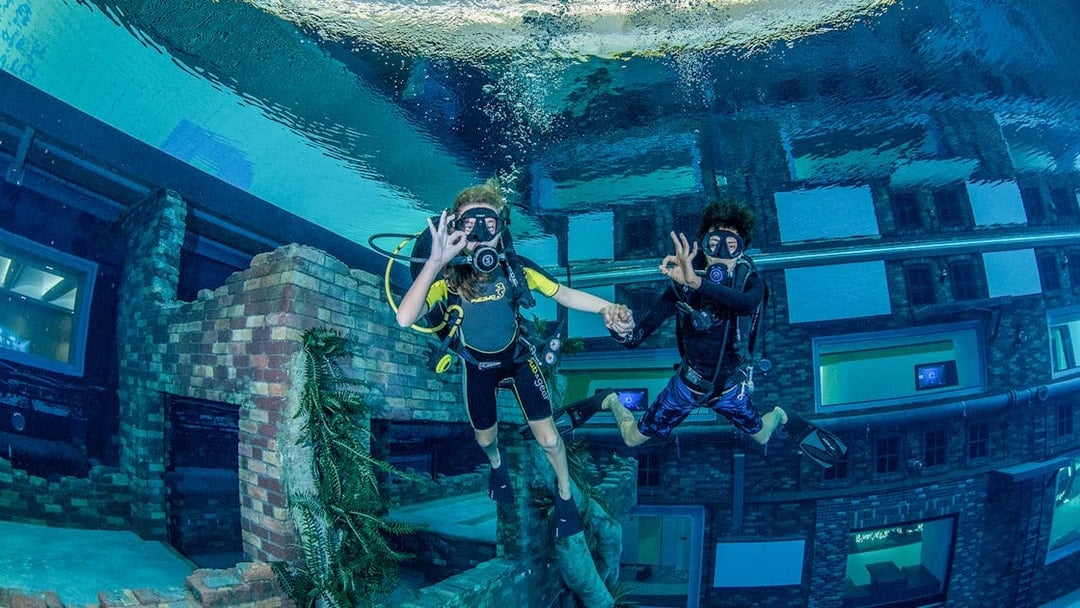 Scuba divers exploring underwater cityscape at Deep Dive Dubai.