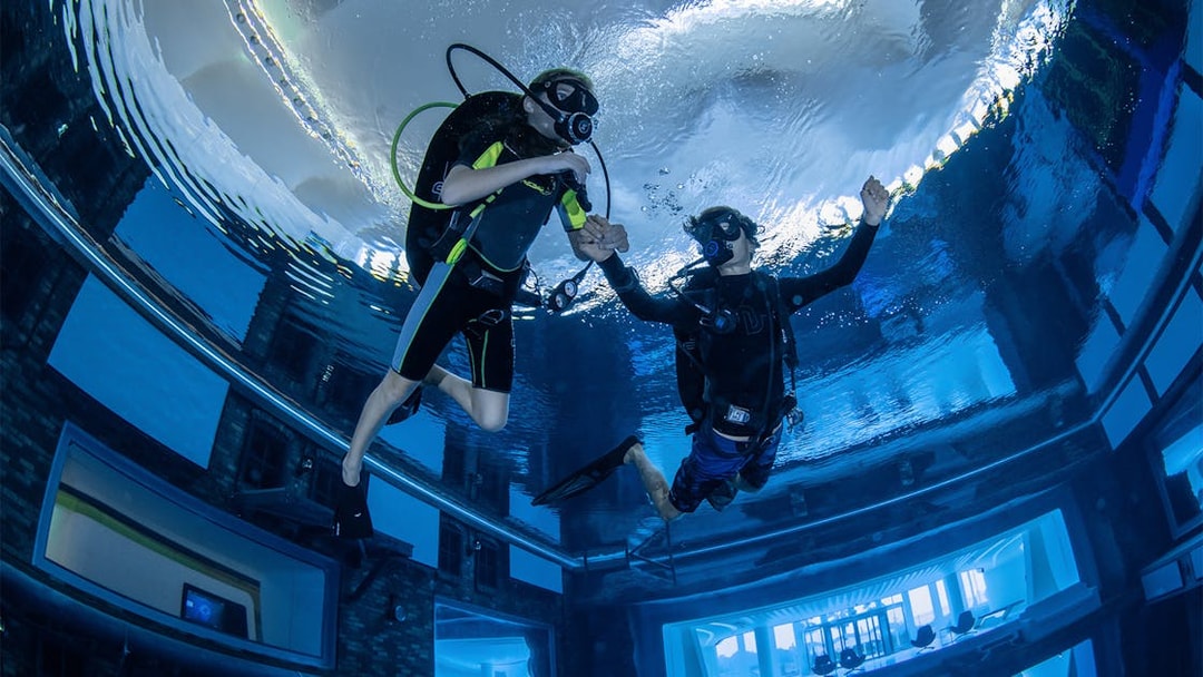 Scuba divers exploring Deep Dive Dubai's underwater city.