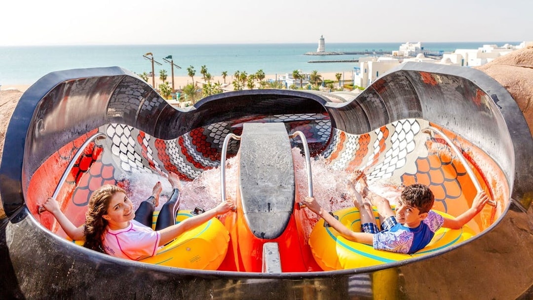 Riders on King Cobra water slide in Doha with ocean view in background.