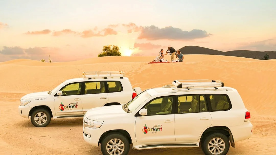 Desert safari with SUVs and group enjoying picnic at sunset.