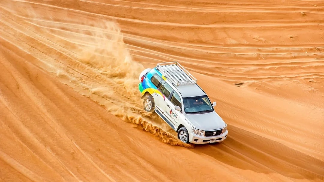 SUV driving through desert dunes during evening safari tour.
