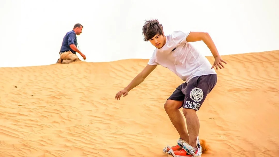 Sandboarding on desert dunes during evening safari experience.
