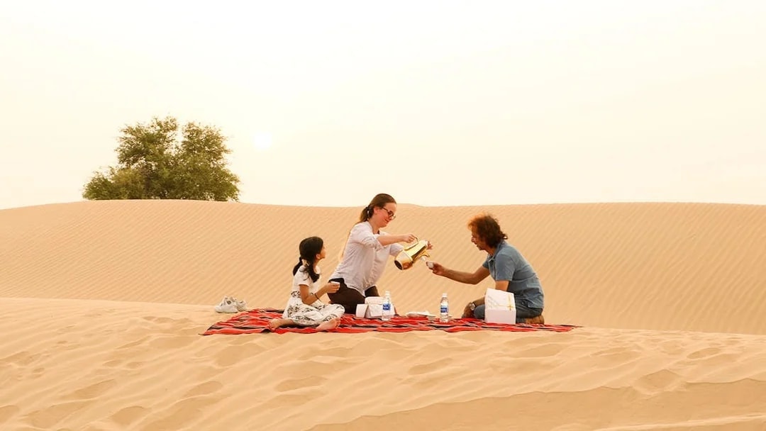 Family enjoying picnic on desert dunes during evening safari.