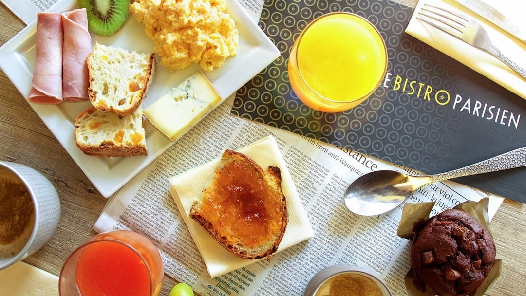 Le Bistro Parisien breakfast spread with ham, cheese, bread, scrambled eggs, and juice.