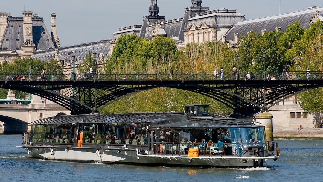 Seine River cruise boat near Paris bridge, with passengers dining, starting at Eiffel Tower.