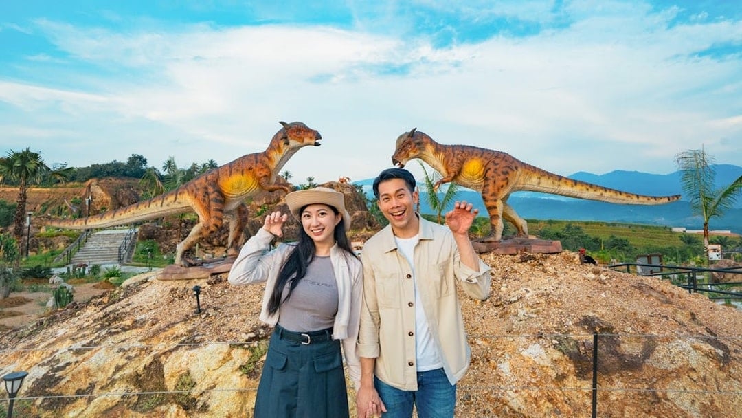 Couple posing with dinosaur sculptures in outdoor park setting.