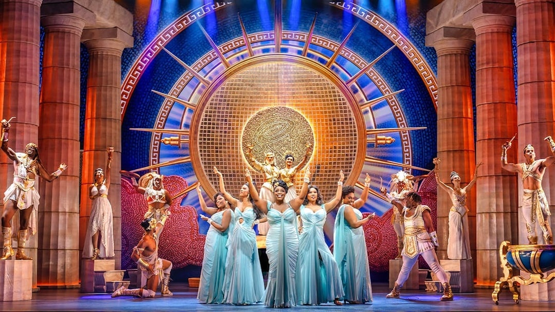 Stage performance of Disney's Hercules with actors in Greek costumes and ornate backdrop.
