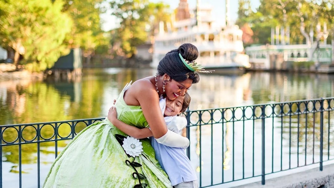 Child hugging a princess at Disneyland Park, California, near a waterfront.