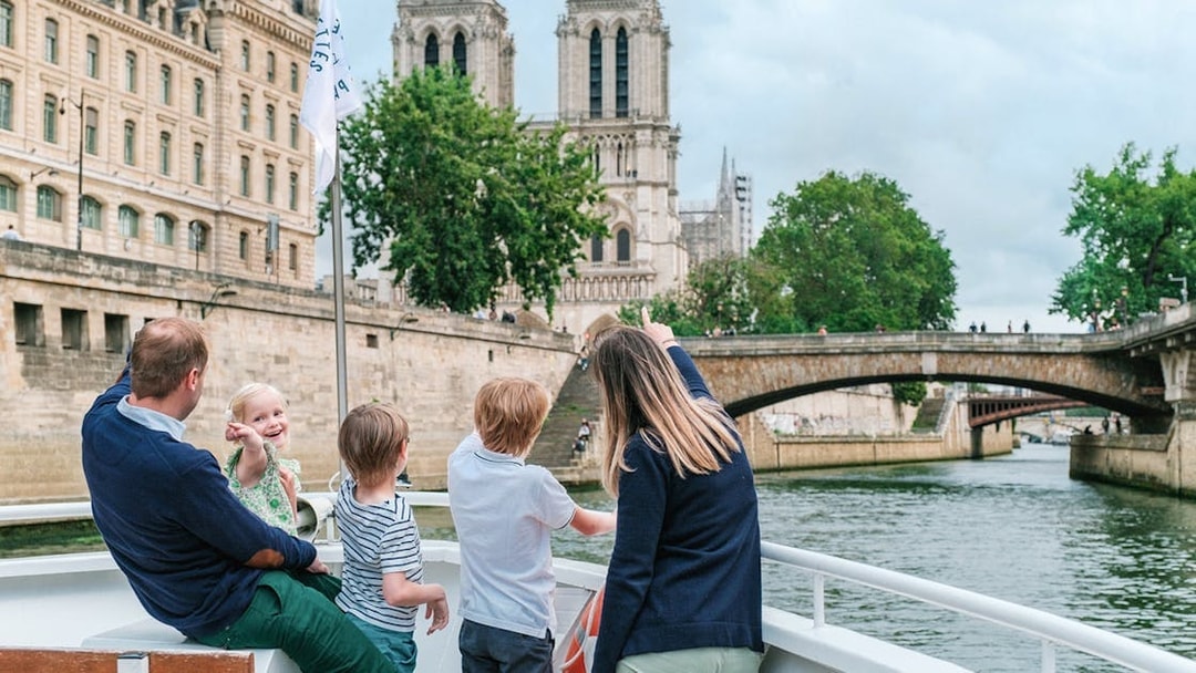 Family enjoying a Seine River cruise with a view of Notre-Dame Cathedral in Paris.