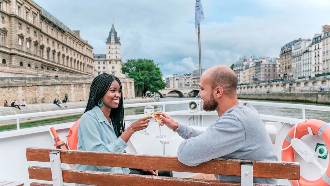 Couple enjoying a Seine River cruise in Paris with historic buildings in the background.