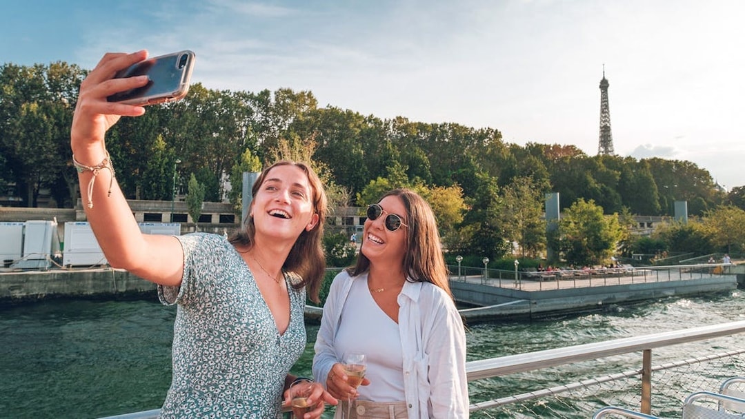 Two people taking a selfie on a Seine River cruise with the Eiffel Tower in the background.