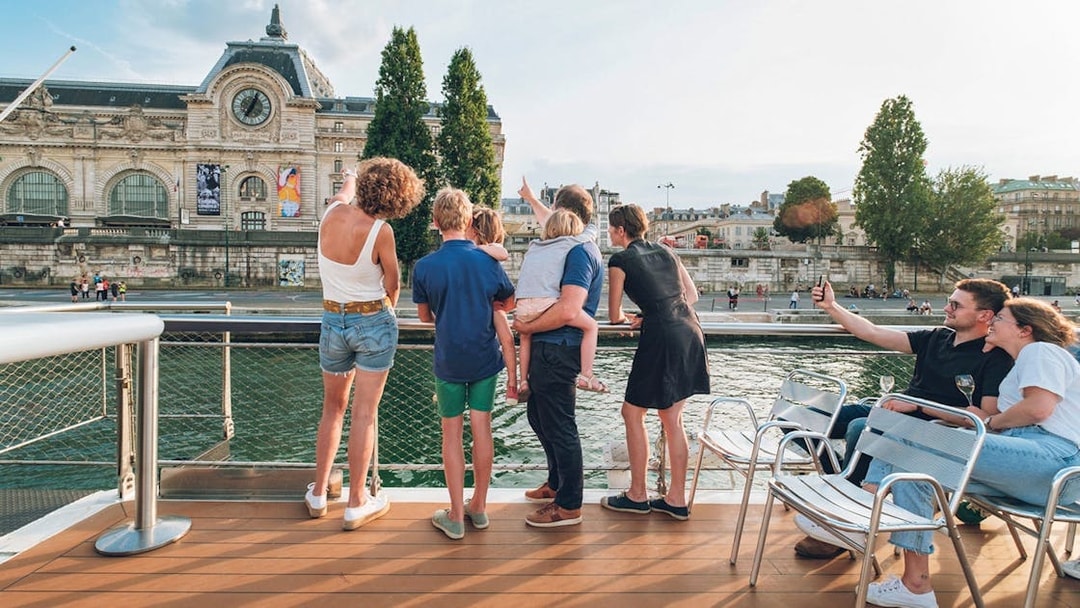 Family enjoying a Seine River cruise with a view of the Musée d'Orsay in Paris.