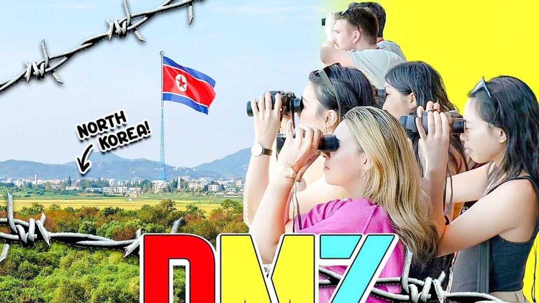 Tour group at DMZ observatory using binoculars to view North Korean village and flag.