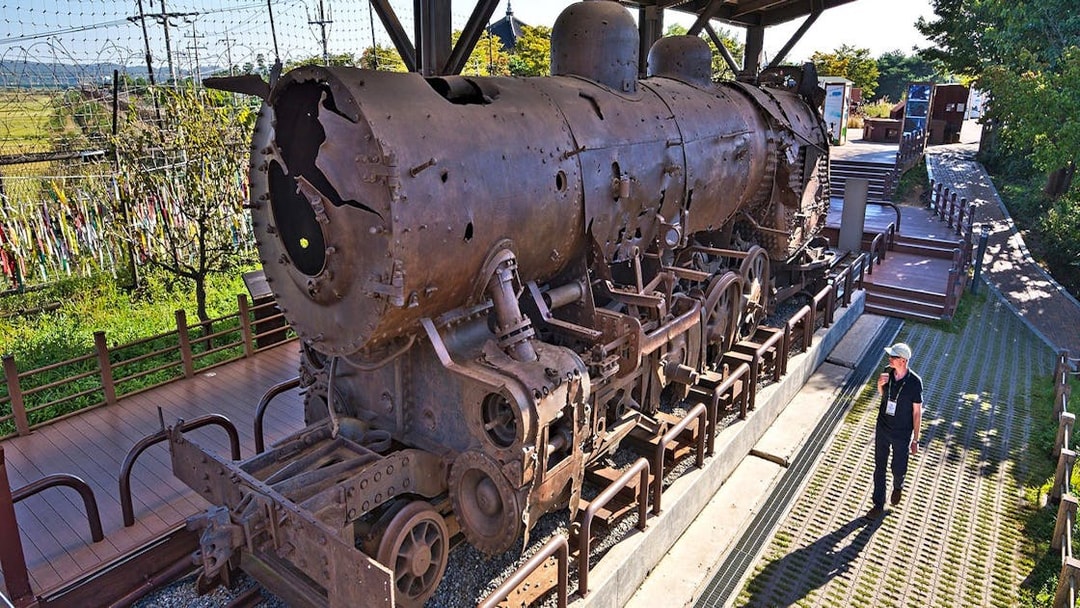 Rusty locomotive at DMZ, South Korea, with barbed wire fence and colorful ribbons in the background.