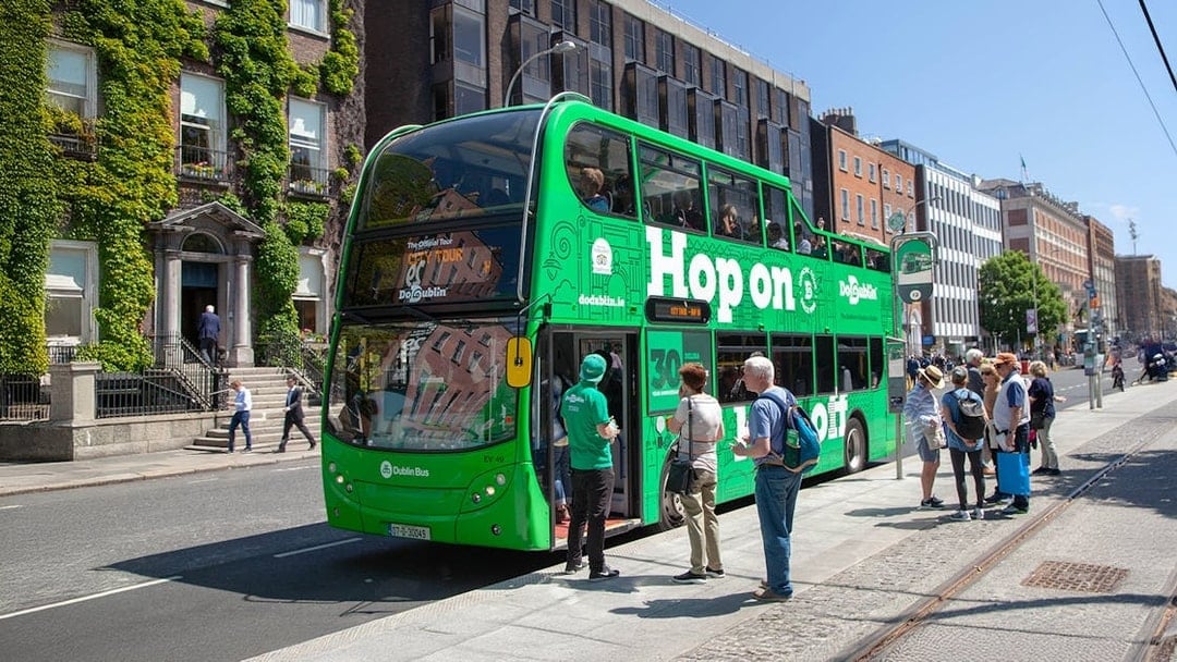 Tourists boarding a green Hop on Hop off bus in Dublin city center.