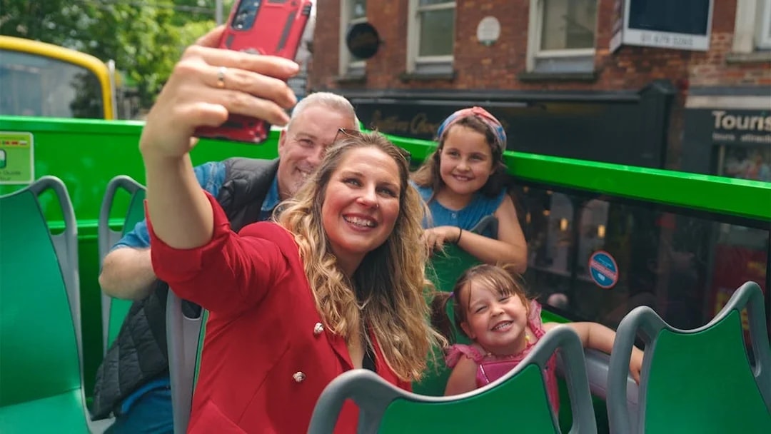 Family taking a selfie on a hop-on hop-off bus tour in the city.