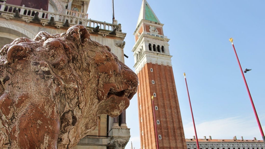 Lion statue near Doge's Palace with St. Mark's Campanile in Venice, Italy.