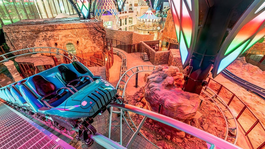 Roller coaster track inside Doha Quest Theme Park with vibrant lights and rocky landscape.