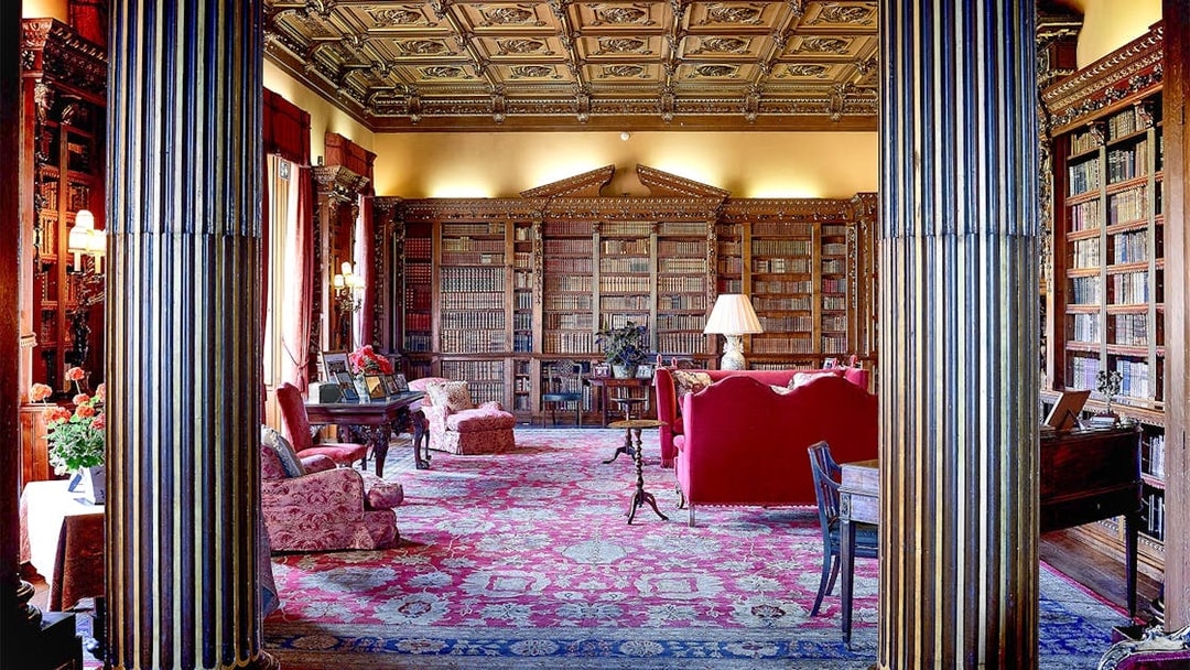 Highclere Castle library with ornate ceiling, bookshelves, and red furnishings.