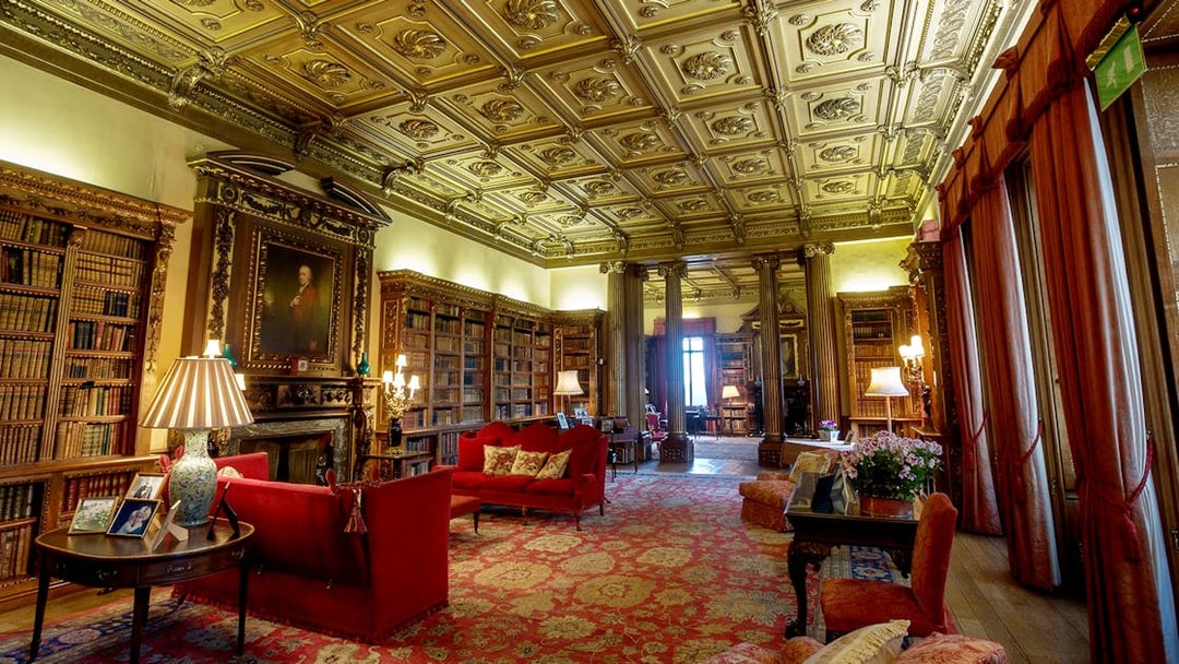Highclere Castle library with ornate ceiling, bookshelves, and red sofas on Downton Abbey tour.