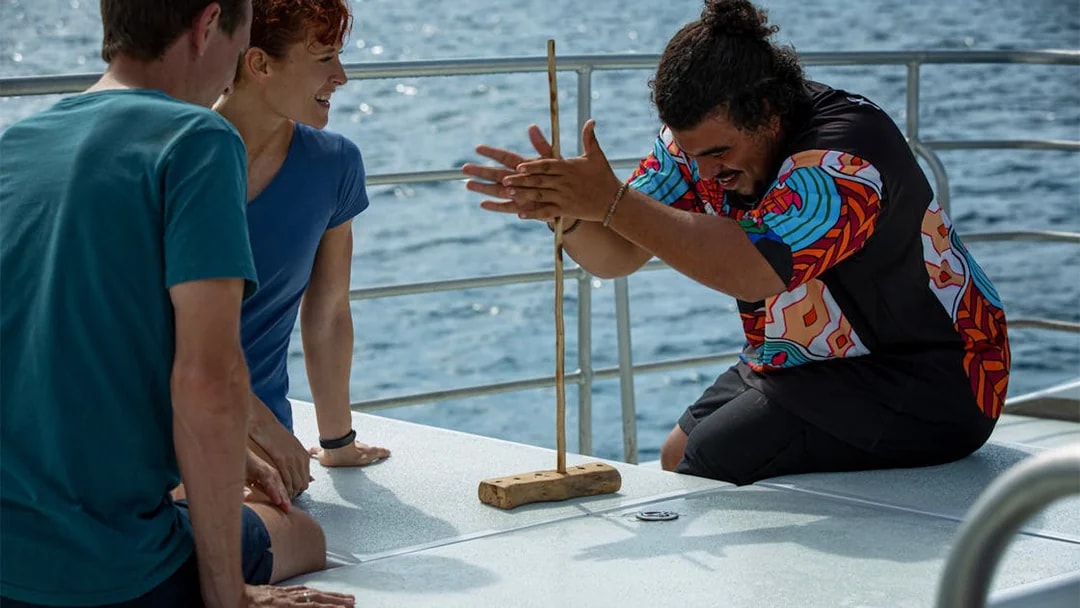 Participants learning traditional fire-starting on Dreamtime Dive & Snorkel tour from Cairns.
