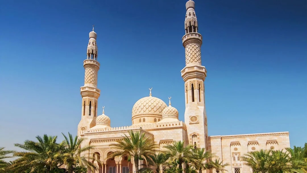 Jumeirah Mosque with palm trees under a clear blue sky in Dubai.