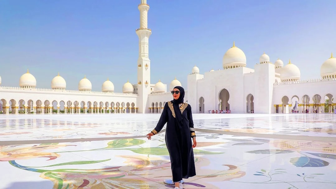Sheikh Zayed Grand Mosque courtyard in Abu Dhabi with a visitor walking.