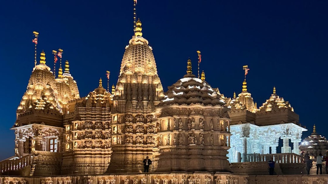 BAPS Hindu Temple illuminated at night, intricate carvings visible, Dubai tour.