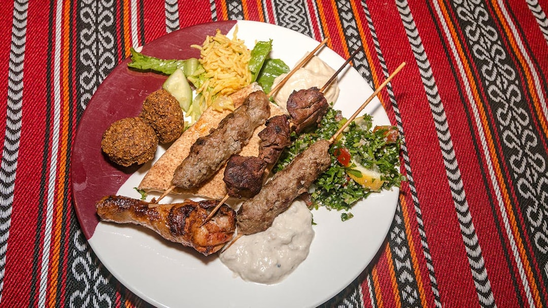 Grilled lamb and beef skewers with chicken, falafel, tabouli, and hummus on a desert safari dinner plate.