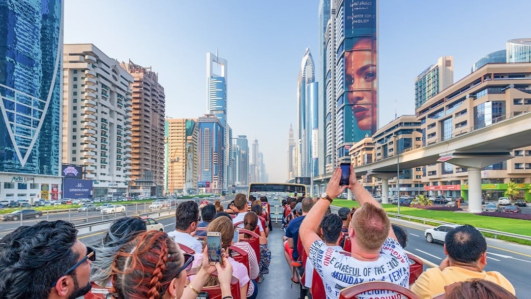 Tourists on a Dubai hop-on hop-off bus tour capturing city skyscrapers along Sheikh Zayed Road.