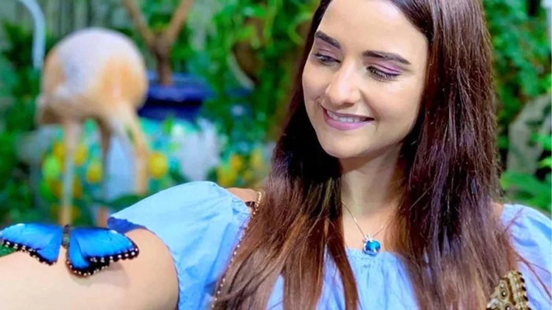 Woman smiling at a blue butterfly on her arm at Dubai Butterfly Garden.