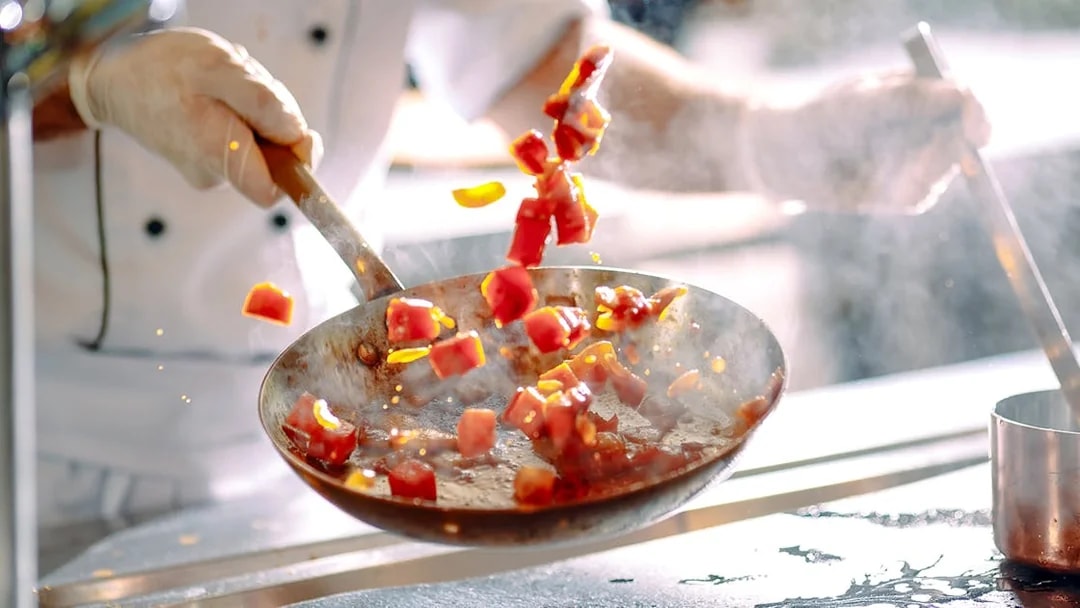 Chef stir frying colorful vegetables in a pan.