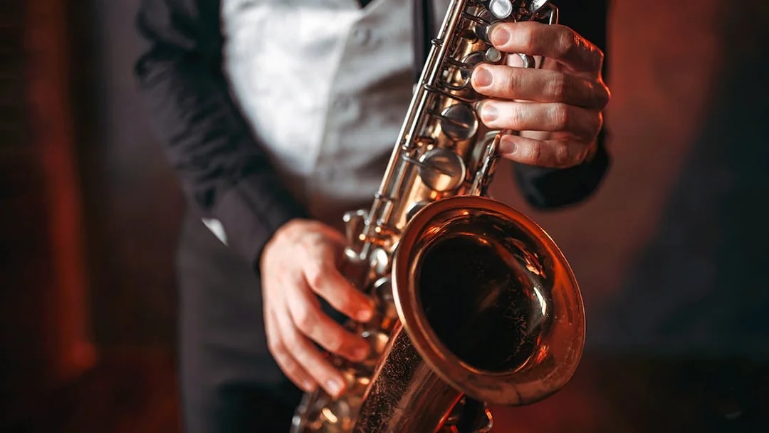 Saxophonist playing a brass saxophone in a dimly lit setting.