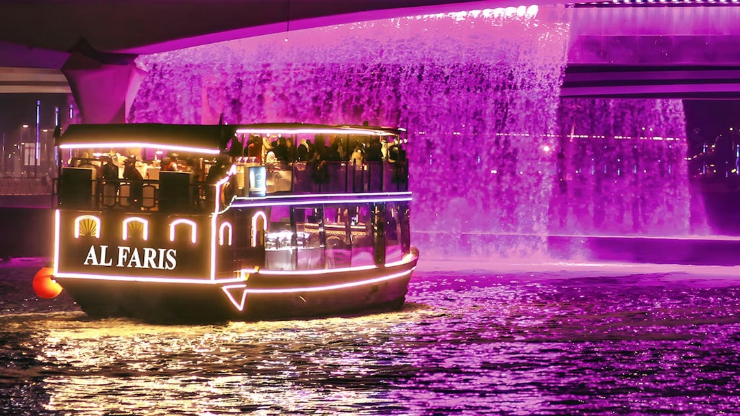 Dubai Water Canal cruise boat with illuminated lights under a purple waterfall.