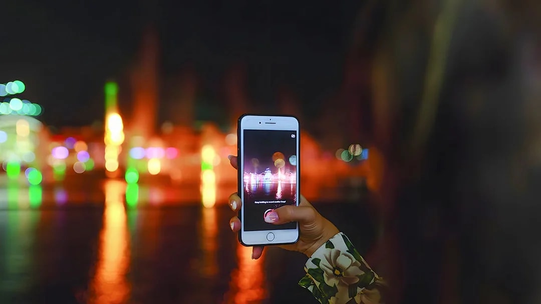 Hand holding a phone capturing Dubai Water Canal lights during dinner cruise.