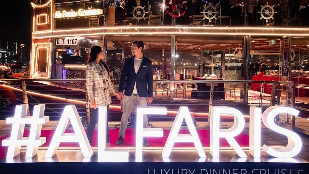 Couple on Dubai Canal Cruise with illuminated Al Faris sign at night.