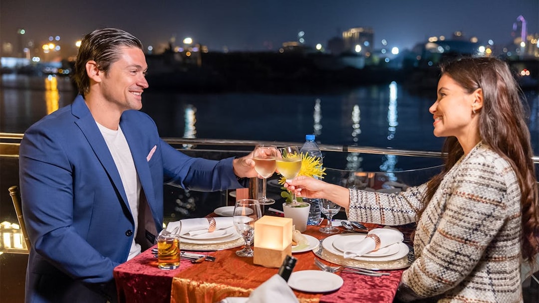 Couple toasting on Dubai Canal cruise at night with city lights in background.