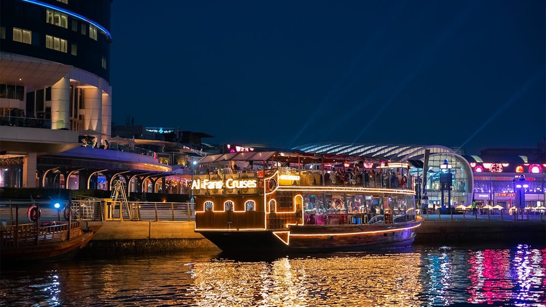 Dubai Canal cruise boat illuminated at night near waterfront buildings.