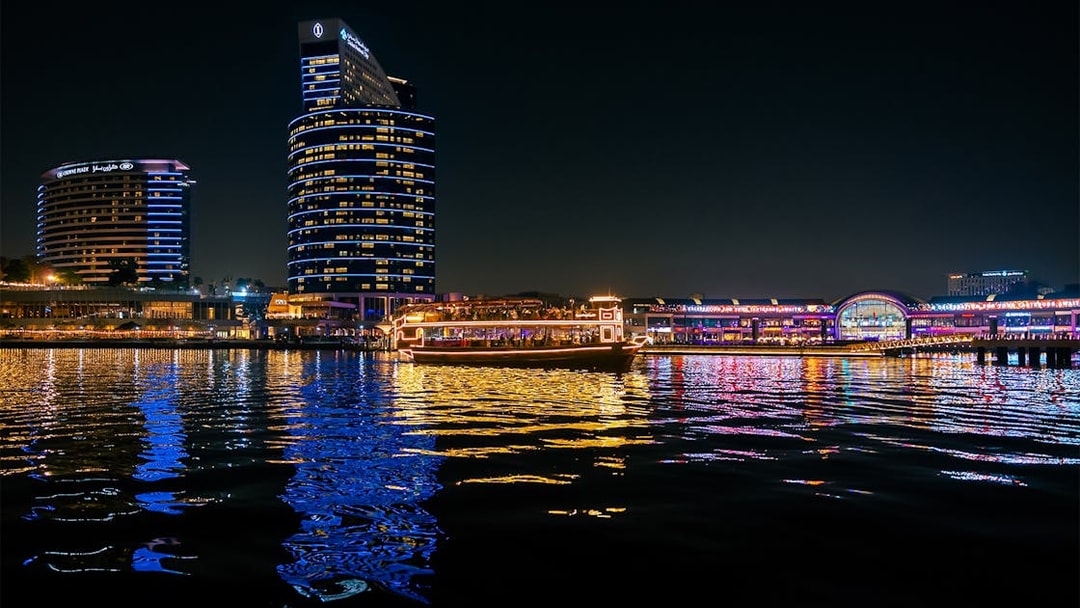 Dubai Canal at night with illuminated cruise boat and city skyline.