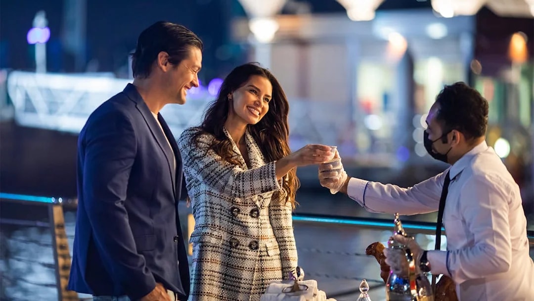 Couple enjoying a drink served by a waiter on a Dubai Canal cruise.