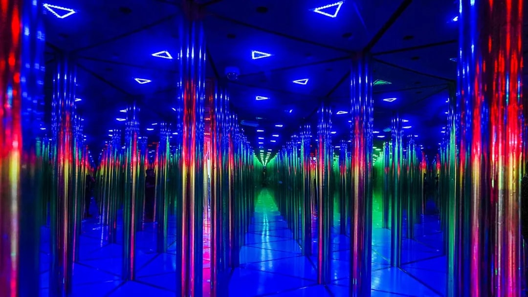 Tourists exploring colorful mirror maze with neon lights.