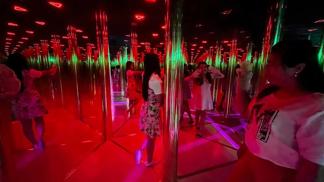 Tourists exploring a colorful mirror maze with reflections and lights.
