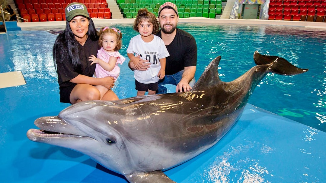 Tourists with children posing beside a dolphin at an aquarium.