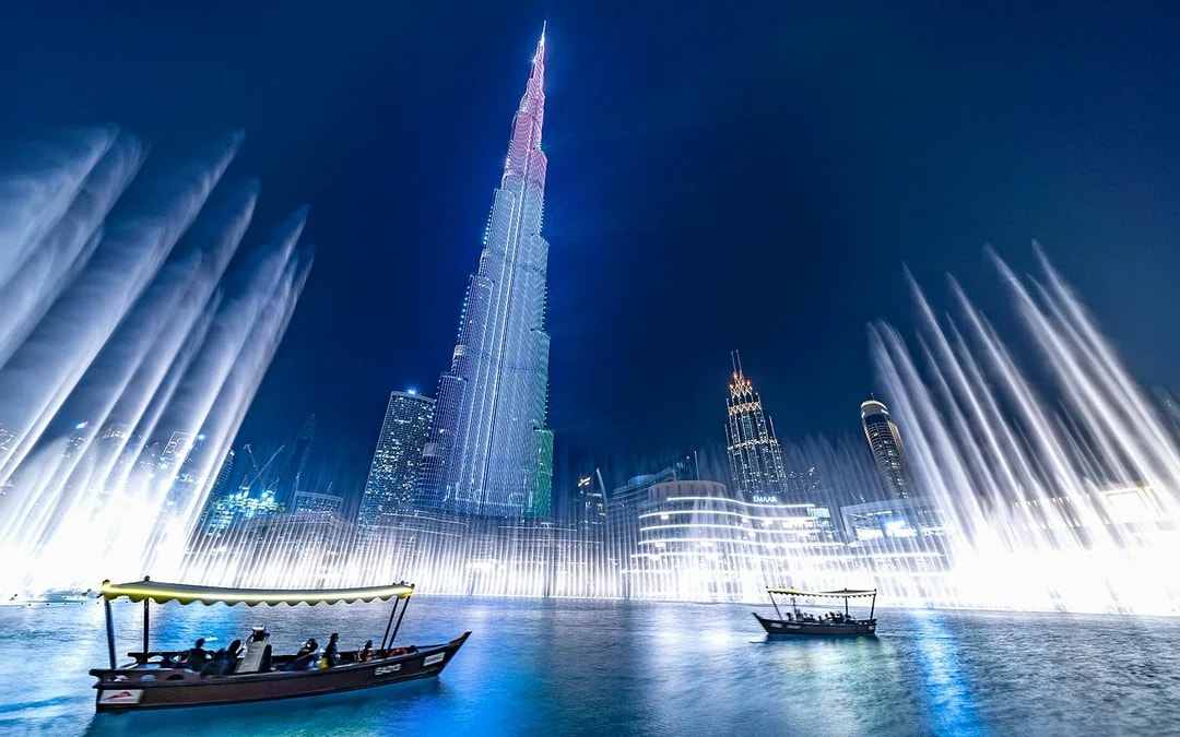 Dubai Fountain show with traditional abra boat on Burj Khalifa Lake at night.