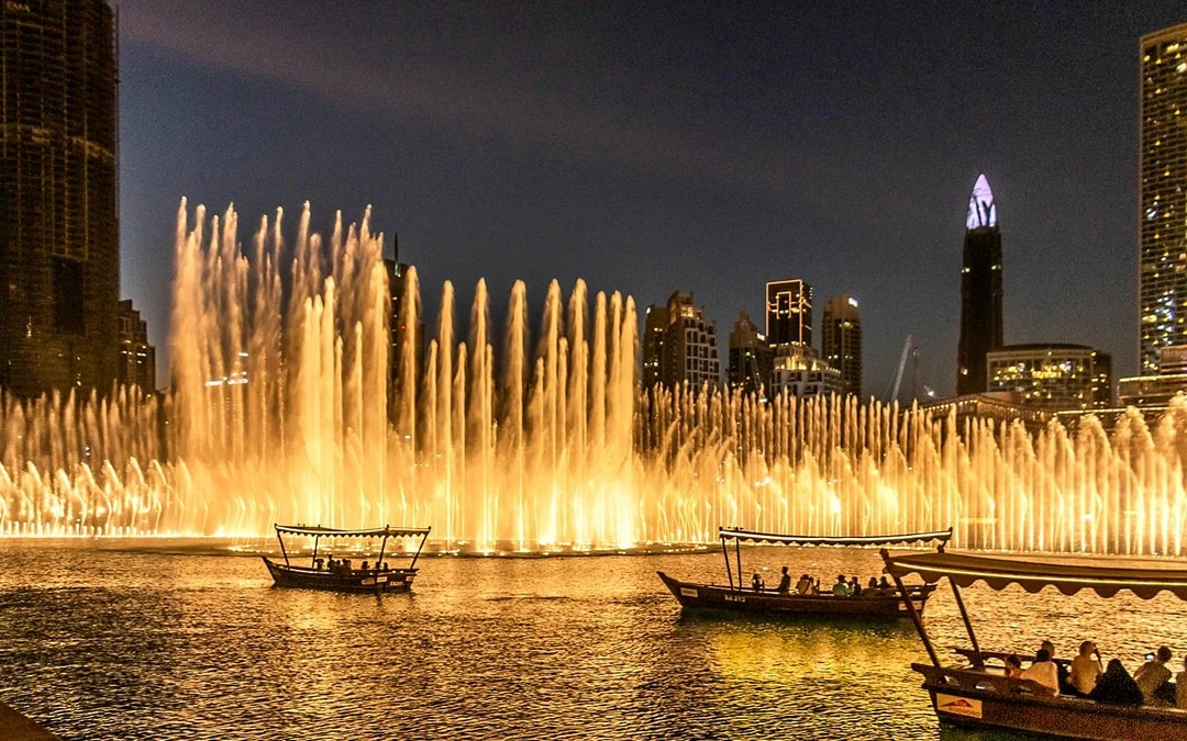 Dubai Fountain Show with traditional abra boats on the lake at night.