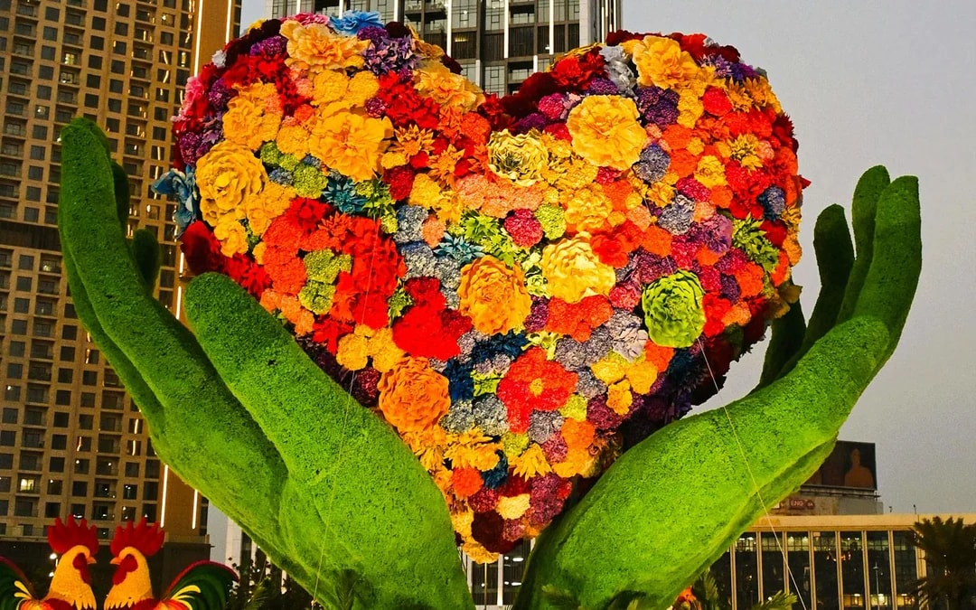 Floral heart sculpture held by green hands at Dubai Garden Glow.
