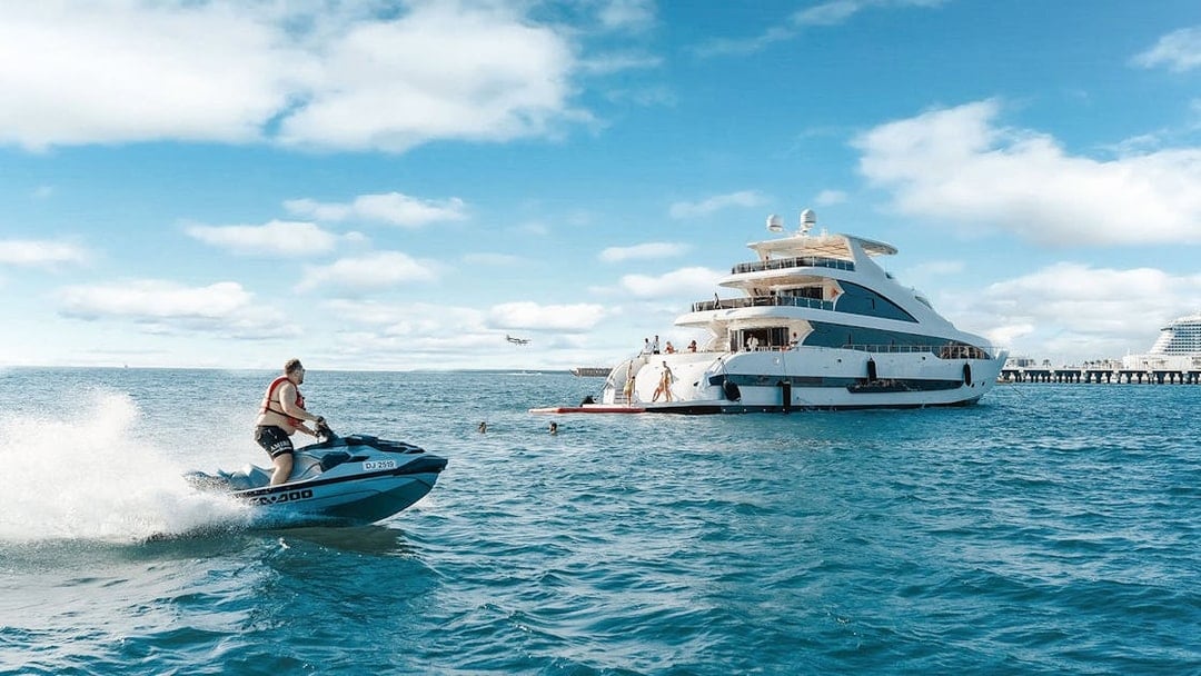 Jet ski near a TriDeck superyacht cruise with people enjoying the water.