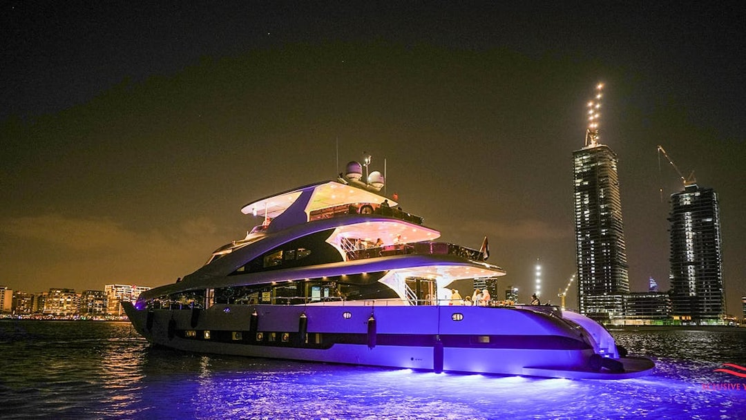 Superyacht cruising near Dubai Marina at night with city skyline in background.