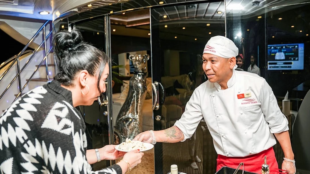 Tourist receiving pasta from chef on Superyacht TriDeck Cruise.