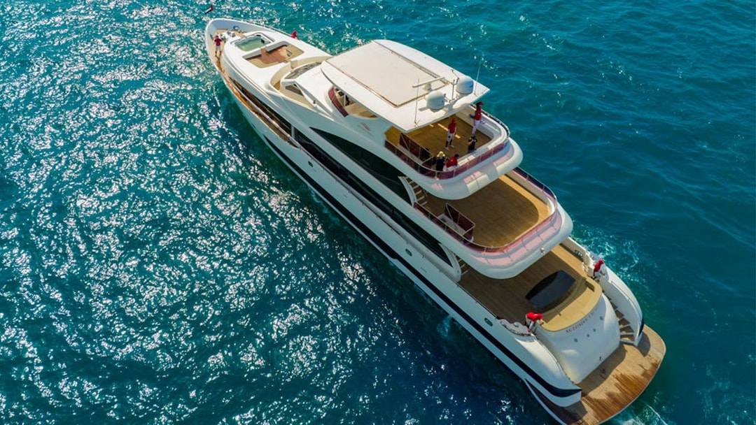 SuperYacht cruising on clear blue waters with people on deck.